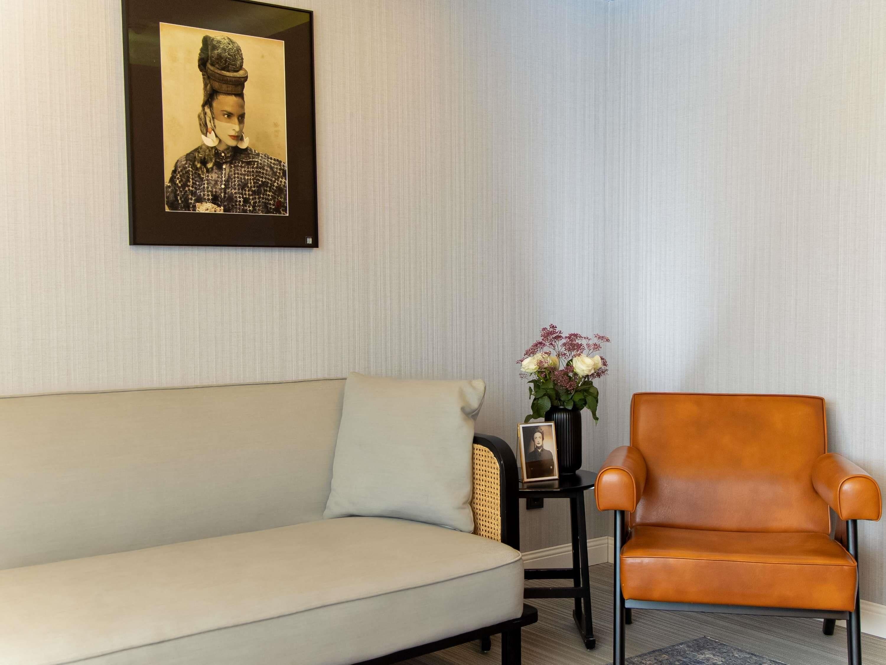 Une pièce comprenant un canapé, un fauteuil, un tableau encadré au mur et une petite table sur laquelle est posé un vase de fleurs.