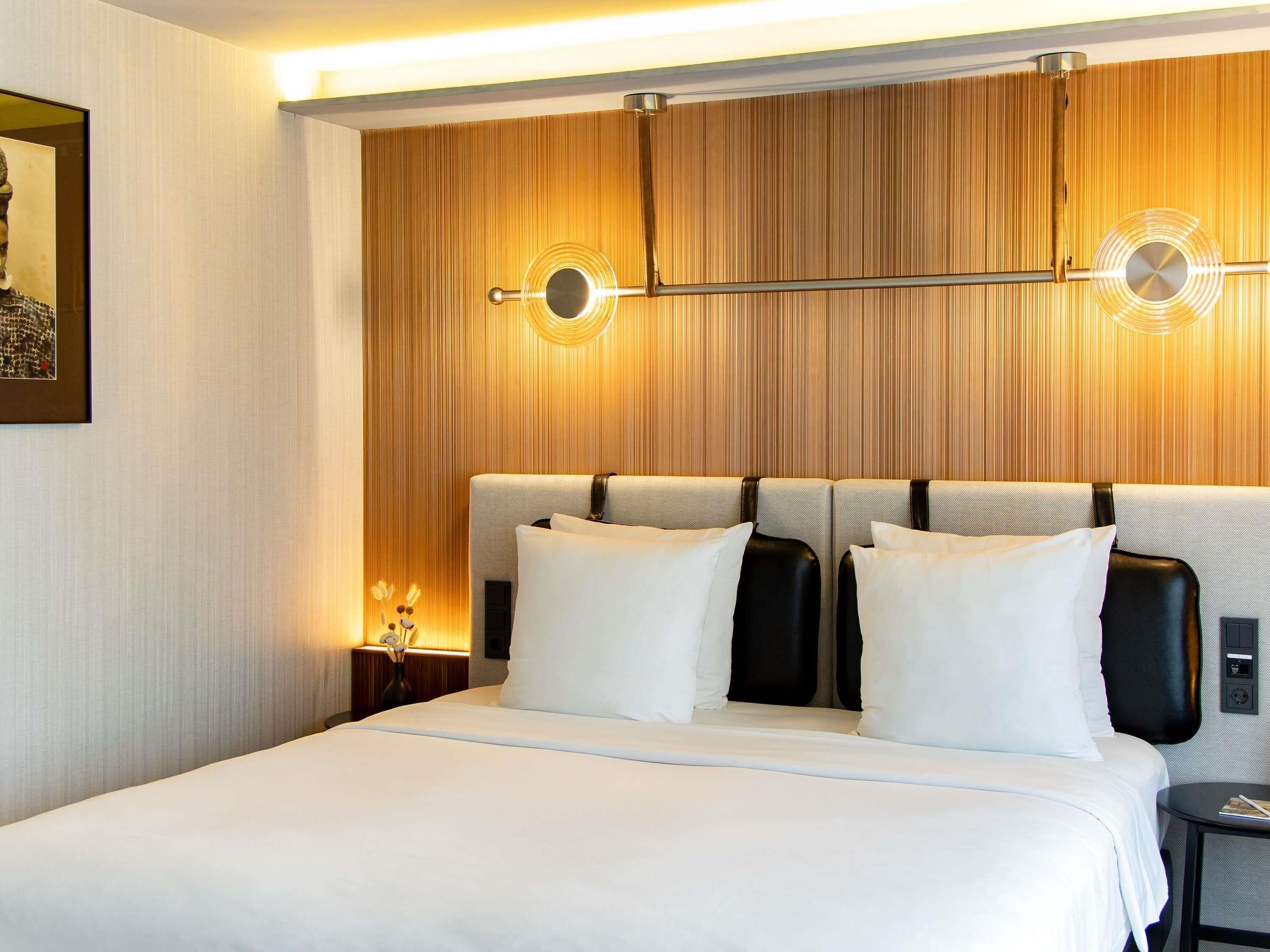 Une chambre d’hôtel avec un grand lit, une tête de lit dotée d’un luminaire et un tableau encadré au mur.