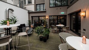 A modern outdoor seating area with tables and chairs, potted plants, and a staircase leading to an upper level. - MUZE Hotel Düsseldorf - Handwritten Collection (Düsseldorf)