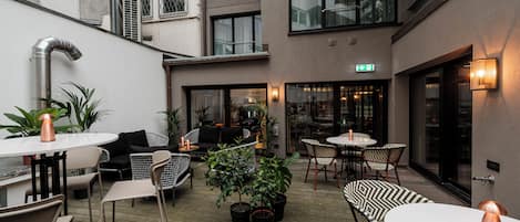 A modern outdoor seating area with tables and chairs, potted plants, and a staircase leading to an upper level.