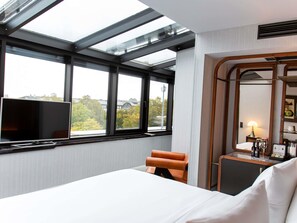 Una habitación de hotel con un ventanal grande, una cama, una silla, un escritorio y un espejo.