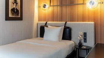 A hotel room with a bed, a nightstand, a vase with flowers, and a framed picture on the wall.