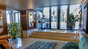 A modern hotel lobby with a large mirror, a blue patterned rug, a green sofa, and a staircase leading to a balcony with outdoor seating. - MUZE Hotel Düsseldorf - Handwritten Collection (Düsseldorf)