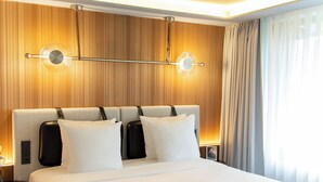 A hotel room with a large bed, a headboard with a light fixture, a nightstand, and a window with curtains. - MUZE Hotel Düsseldorf - Handwritten Collection (Düsseldorf)