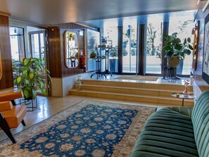 Un hall de hotel con alfombra de diseño azul, un sofá verde y una escalera que conduce a un balcón con vistas a la calle.