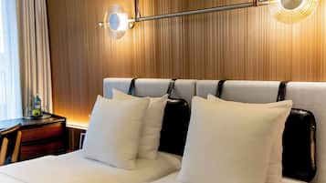 A hotel room with a wooden headboard, two beds with white and black headboards, and a nightstand with a bottle and glasses.