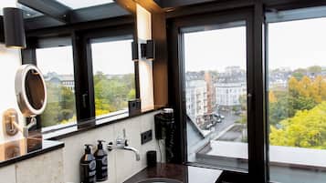 A modern bathroom with a large window, a round mirror, a sink, and two bottles of shampoo.