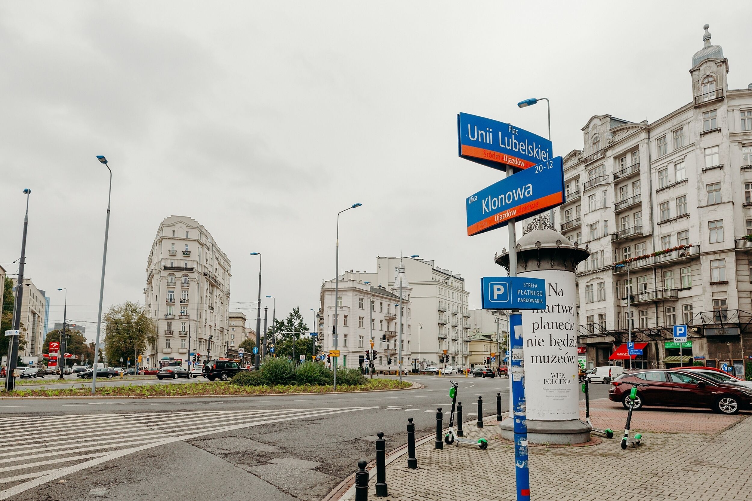 A city intersection with directional signs, a roundabout, and historic buildings.