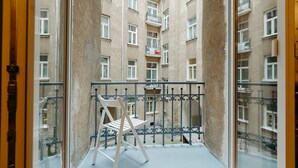 Un balcón con una silla, baranda de metal y vista a un edificio de varios pisos con balcones.