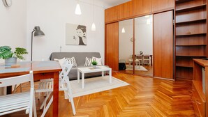 Un salón moderno con suelo de madera, muebles blancos, un sofá gris y un armario de madera.