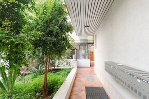 A corridor with a tiled floor, a metal fence, and a tree.