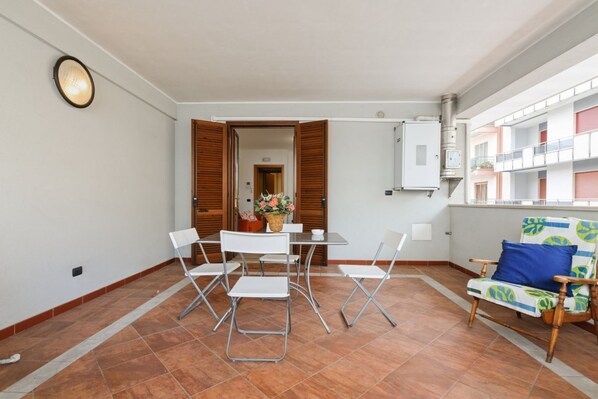 A dining area with a table and chairs, a window with a view of buildings, and a chair with a cushion.