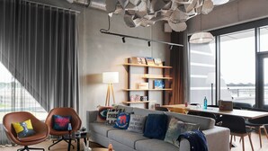 A modern living room with a grey sofa, two armchairs, a coffee table, and a bookshelf. - Moxy Cologne-Bonn Airport (Cologne)