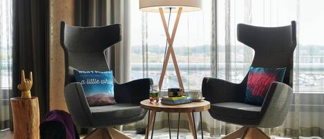 Two modern armchairs with cushions, a small table with a lamp, and a view of a bridge through large windows.
