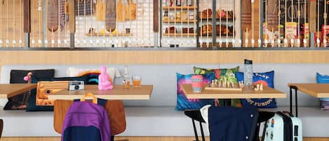A cozy seating area with wooden tables, cushioned benches, and a variety of items on display, including a camera, a pink plush toy, and a chess set.