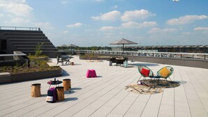 An outdoor seating area with tables, chairs, and a large umbrella. - Moxy Cologne-Bonn Airport (Cologne)