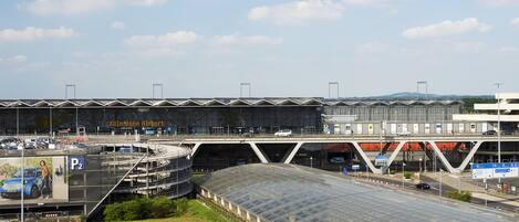 An airport terminal with a large glass roof, a pedestrian bridge, and multiple parking signs.