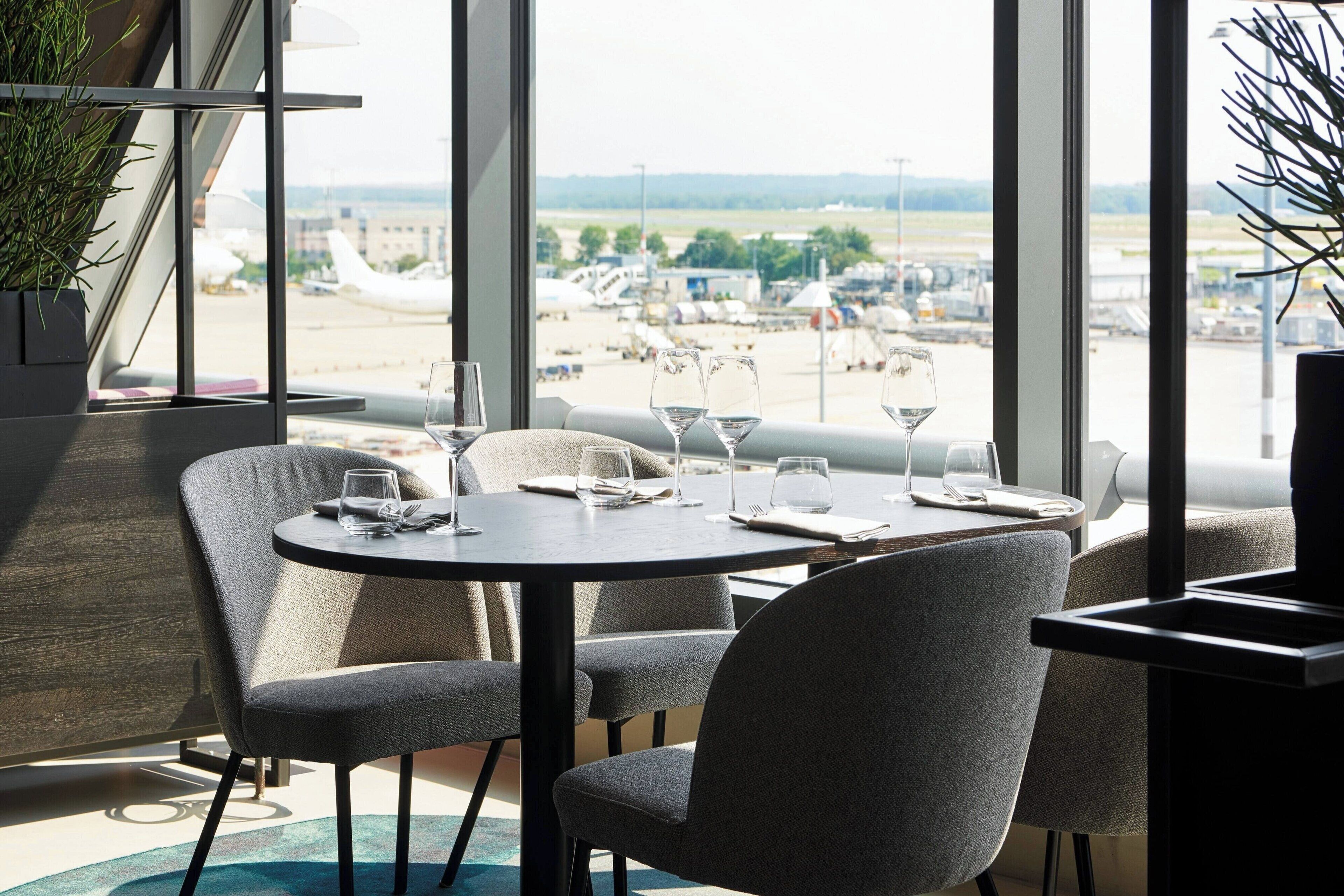 A dining area with a view of an airport, featuring a round table with chairs and a potted plant.