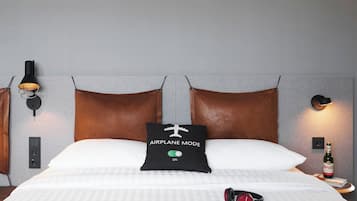 Una habitación de hotel con una cama, un almohadón con la inscripción 'AIRPLANE MODE', una botella de cerveza y auriculares sobre la cama.