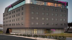 A modern hotel with a curved facade, large windows, and a neon sign. - Moxy Cologne-Bonn Airport (Cologne)