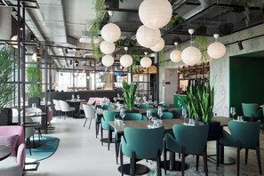 A modern restaurant with teal chairs, white tablecloths, and hanging paper lanterns. - Moxy Cologne-Bonn Airport (Cologne)