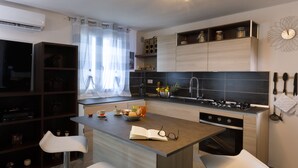 A modern kitchen with a central island, two bar stools, a built-in oven, and a variety of kitchen utensils on the wall.