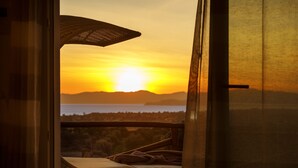 A room with a view of the sunset over the ocean, wicker furniture, and a large window.