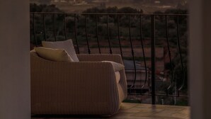 A wicker sofa with cushions, a view of the ocean, and a mountainous landscape in the background.