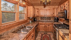 A wooden cabin kitchen with granite countertops, stainless steel appliances, and a chandelier. - ⛰️Tuscan Vista🍃Pet Friendly, Fenced Yard, Single-Level, Hot Tub & Game Room (Sevierville)