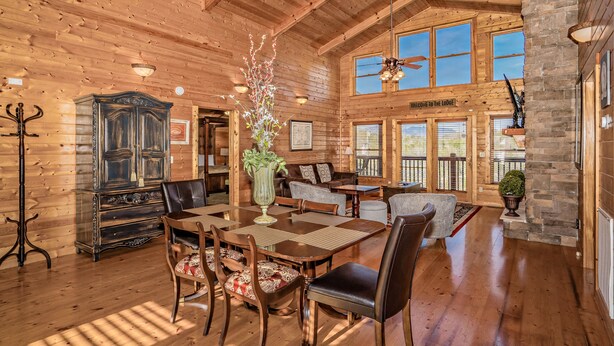 A spacious wooden lodge interior with a dining area, a large wooden cabinet, and a stone fireplace. - ⛰️Tuscan Vista🍃Pet Friendly, Fenced Yard, Single-Level, Hot Tub & Game Room (Sevierville)