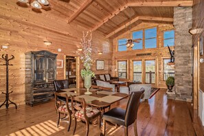 A spacious wooden lodge interior with a dining area, a large wooden cabinet, and a stone fireplace. - ⛰️Tuscan Vista🍃Pet Friendly, Fenced Yard, Single-Level, Hot Tub & Game Room (Sevierville)