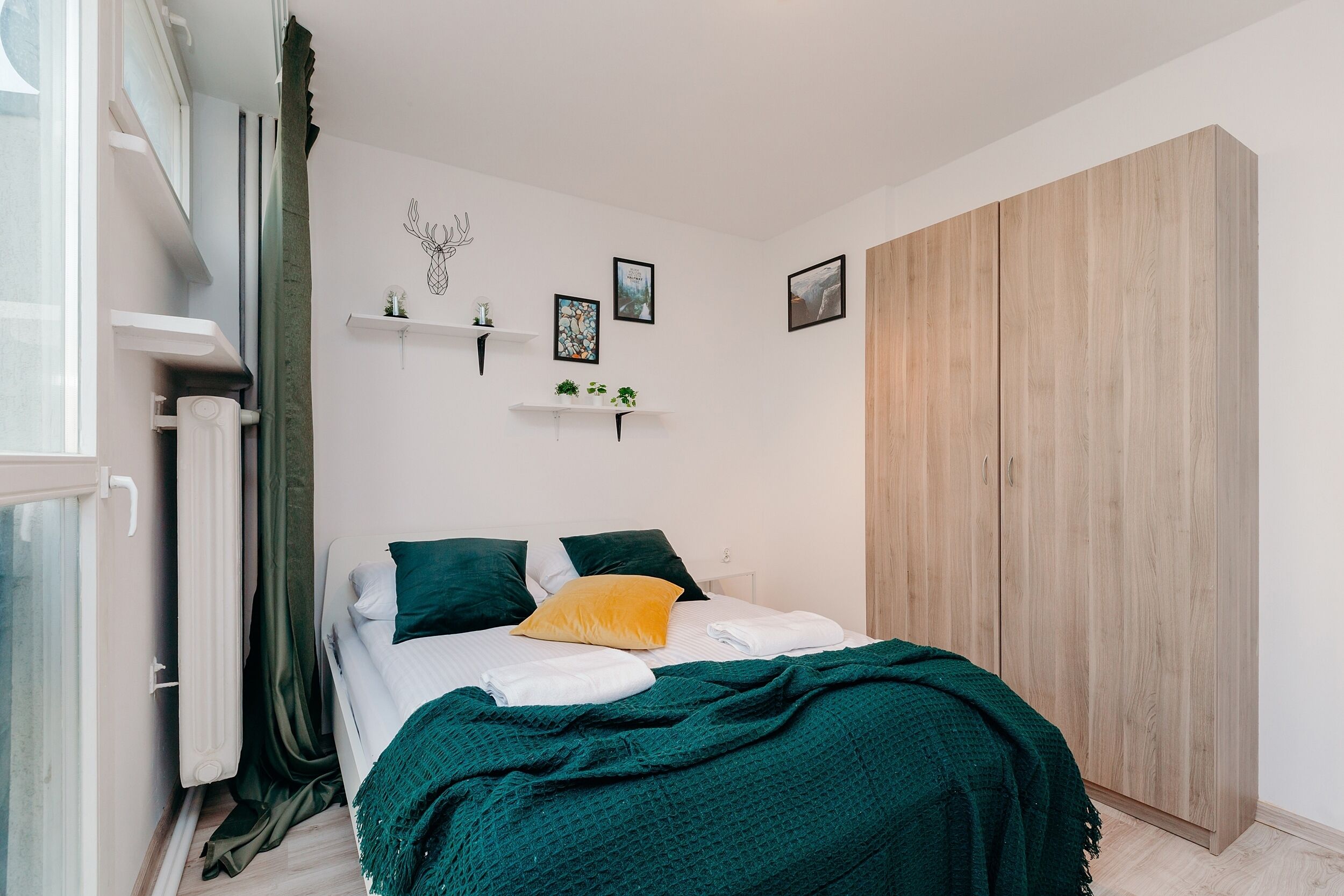 Ein Schlafzimmer mit einem Bett, einem Kleiderschrank und Regalen an der Wand mit Dekorationselementen.