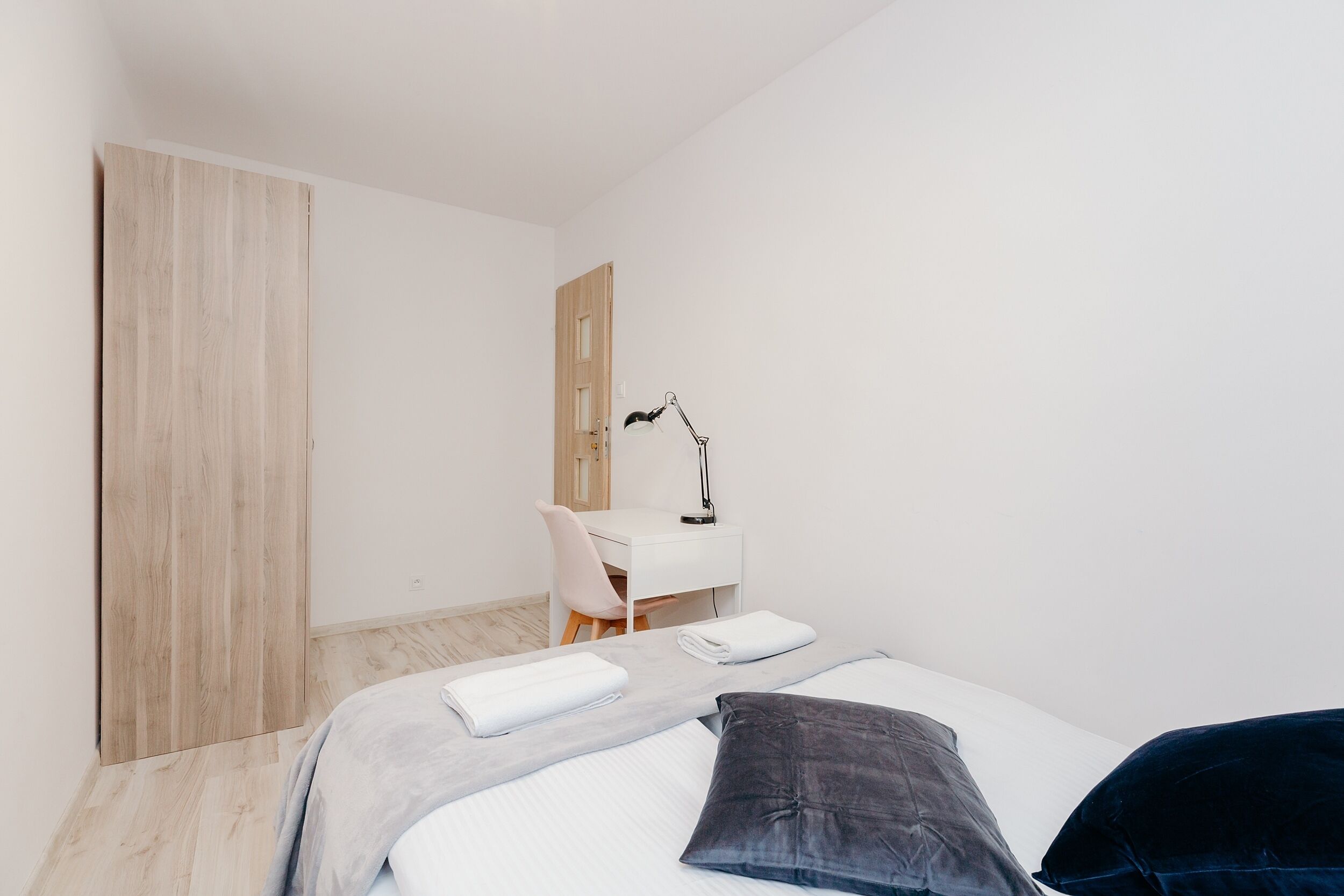 A minimalist hotel room with a bed, a desk, and a chair.