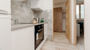 A modern kitchen with white cabinets, a built-in oven, and a stainless steel range hood. A wooden door leads to another room. - ShortStayPoland Krochmalna B17 (Warsaw)
