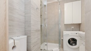A modern bathroom with a glass-enclosed shower, a toilet, and a built-in washing machine. - ShortStayPoland Krochmalna B17 (Warsaw)