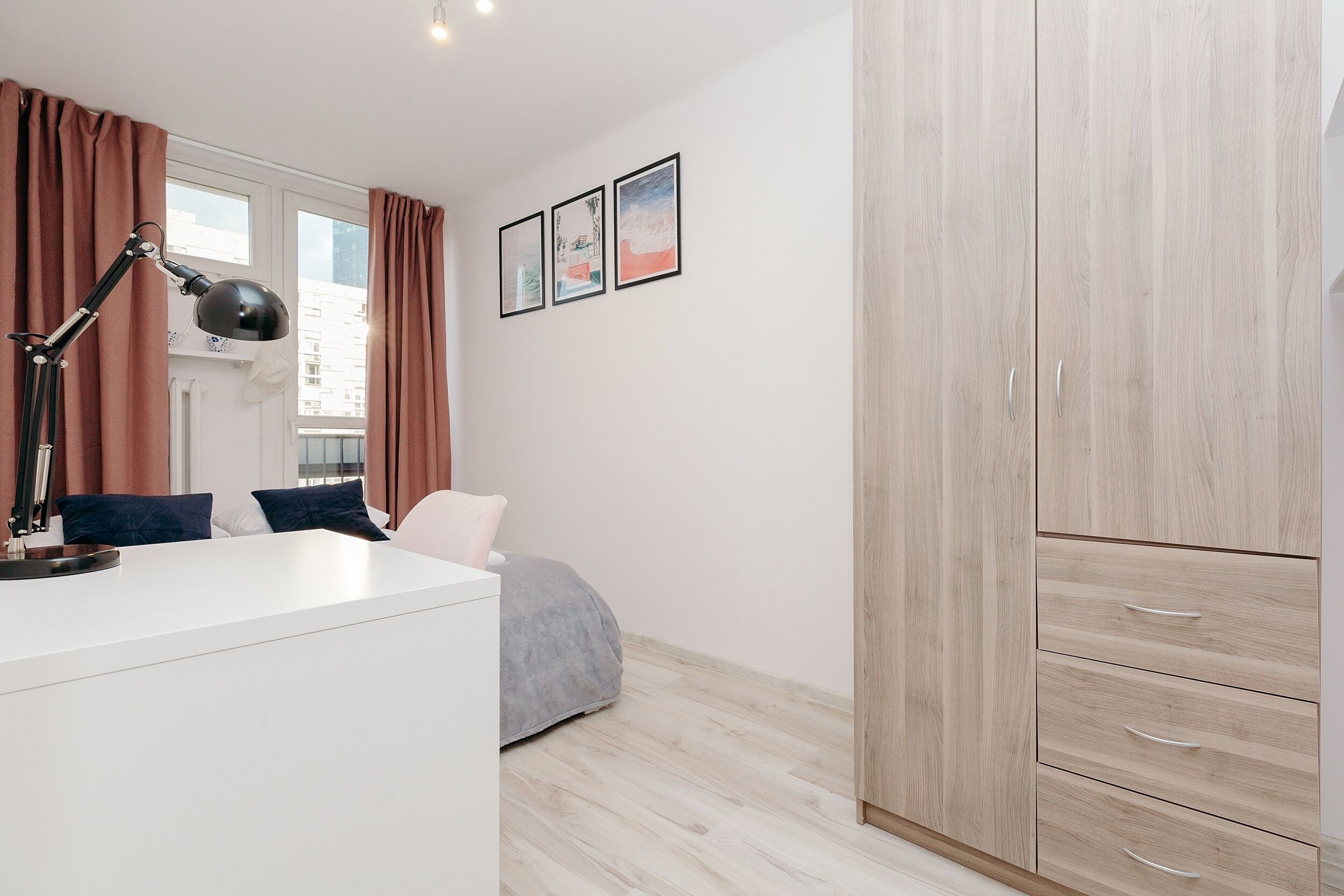A bedroom with a bed, bedside table, lamp, wardrobe, and window with curtains.
