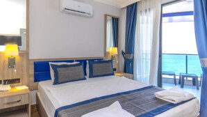 Habitación de hotel con una cama grande, una mesita de noche con lámpara, una ventana con cortinas y vistas al mar.