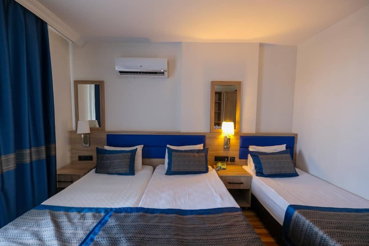 A hotel room with two beds, a nightstand, a lamp, an air conditioner, and a window with curtains.