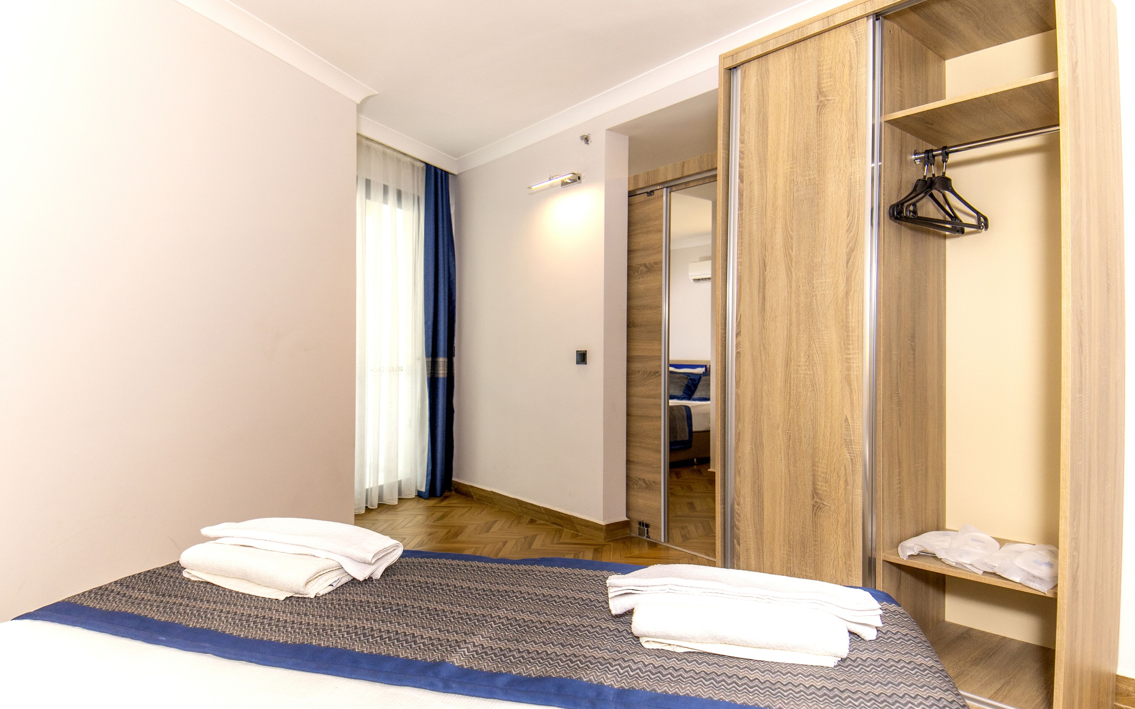 Une chambre d’hôtel avec un lit, une armoire en bois, un miroir et une salle de bain visible à travers une porte.