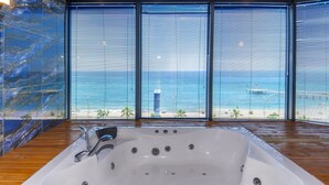 Una bañera grande con vista al océano a través de ventanales del piso al techo.