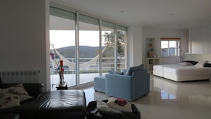 Un salon moderne doté d’une grande porte-fenêtre coulissante donnant sur un balcon, d’un canapé, d’une table basse et d’un lit avec une tête de lit.