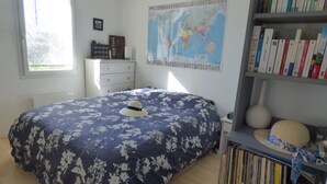 Ein Schlafzimmer mit Bett, Kommode, Bücherregal, einer Karte an der Wand und einem Fenster.