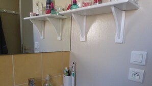 Ein Badezimmer mit einem weißen Waschbecken, einem Spiegel und einem Ablagefach darüber mit Toilettenartikeln.