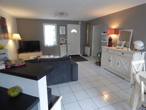 A modern living room with a sectional sofa, a flat-screen TV, a dining area with a table and chairs, and a kitchen area with cabinets and a countertop. - A Bird Paradise (Brem-sur-Mer)