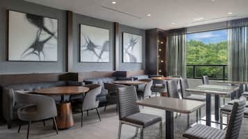 A modern dining area with a mix of booths and tables, large windows with a view of greenery, and abstract art on the walls.