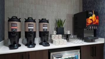 A coffee station with three coffee dispensers, a refrigerator with bottled water, and a fruit juice dispenser.