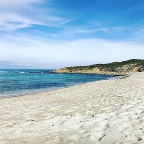 Une plage de sable fin, avec une eau d’un bleu limpide et, au loin, une formation rocheuse.