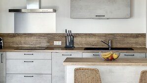 Eine moderne Küche mit einer Edelstahl-Dunstabzugshaube, einem Einbauofen, einer Mikrowelle und einer Holzausziehtafel. In der Küche befindet sich ein Spülbecken mit Armatur, ein Schneidebrett und eine Obstschale.