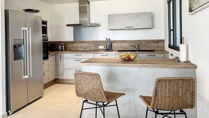 Eine moderne Küche mit Kühlschrank aus Edelstahl, einem eingebauten Ofen, einer Mikrowelle, einer Dunstabzugshaube aus Edelstahl, einer Holz Arbeitsplatte, einer Spüle und zwei Korbstühlen.