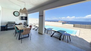 Eine moderne Küche mit Essbereich, ein großes Fenster mit Meerblick und ein Poolbereich mit Sitzgelegenheiten.